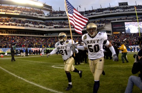 US Navy 031206-N-9693M-532 Navy slot back Tony Lane (21) and line backer Ben Matthews lead the team onto the field holding an American flag prior to the 104th Army Navy Game