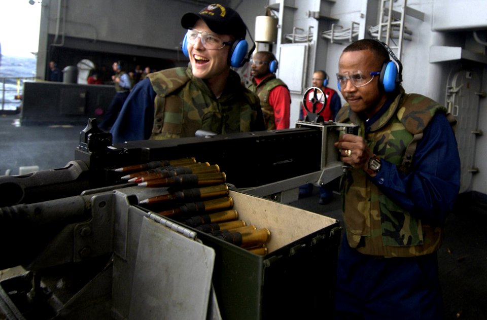US Navy 040125-N-5319A-002 Gunner's Mate 3rd Class Andrew Smith from Weatherford, Texas, looks on as Chief Gunner's Mate Donald Watkins fires a 50. Caliber machine gun off the fantail