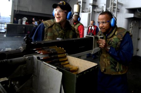 US Navy 040125-N-5319A-002 Gunner's Mate 3rd Class Andrew Smith from Weatherford, Texas, looks on as Chief Gunner's Mate Donald Watkins fires a 50. Caliber machine gun off the fantail