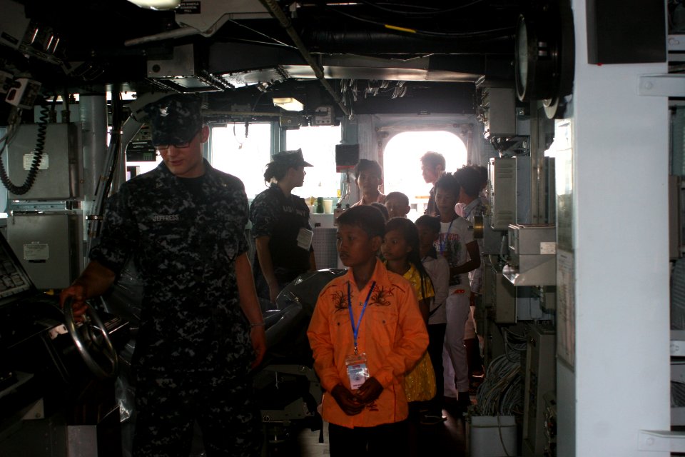 US Navy 101204-N-4780J-024 Cyptologic Technician 3rd Class Michael Jeffress shows local children the ship's helm during a tour aboard the guided-mi
