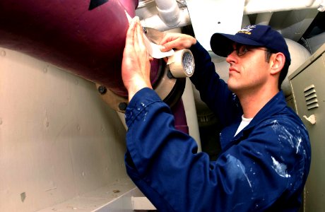 US Navy 040322-N-2143T-001 Airman George Ogle, of Tucson, Ariz., covers piping with tape before painting spaces aboard the nuclear powered aircraft carrier USS Nimitz (CVN 68) photo