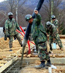 US Navy 040324-N-0000X-001 Construction Electrician 2nd Class Juan Perez signals a concrete pump truck operator as he skillfully places concrete in the foundation forms for a latrine facility photo