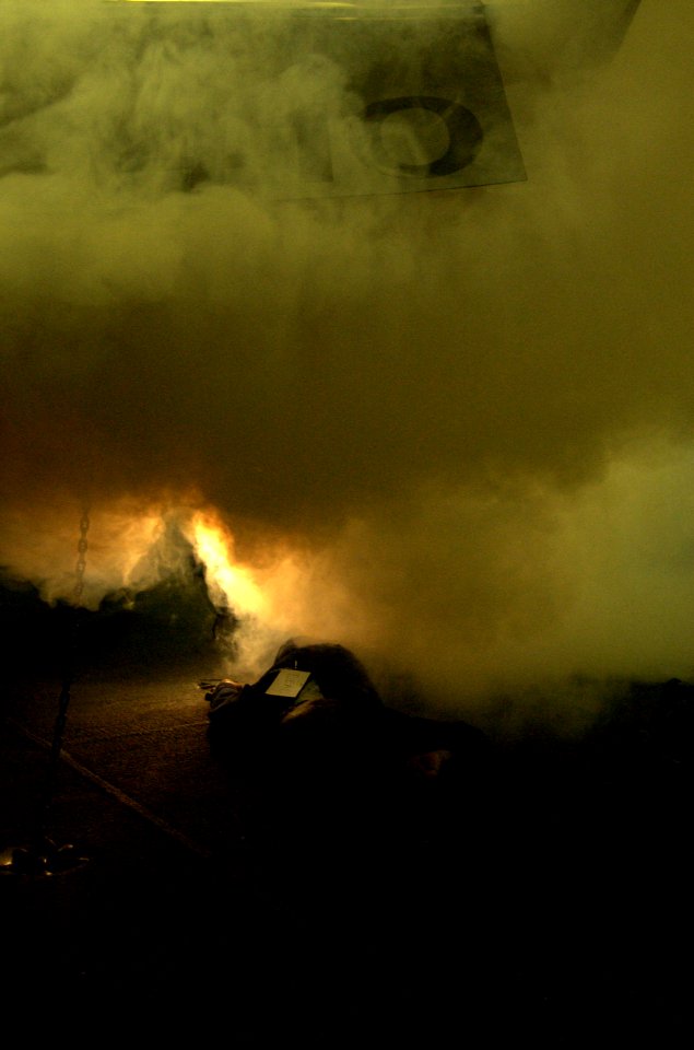 US Navy 040309-N-5319A-001 Simulated smoke pours over a sailor as he plays the role of a casualty member during an Improvised Explosive Device (IED) drill and Mass Causality exercise in the hangar bay aboard USS George Washingt