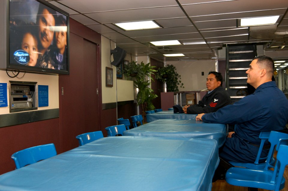 US Navy 040324-N-9860Y-039 Machinist's Mate 1st Class William Velasco, from Batanes, Philippines, watches American Idol as a family portrait of himself and his daughters is broadcast prior to the elder daughter, Camile Velasco
