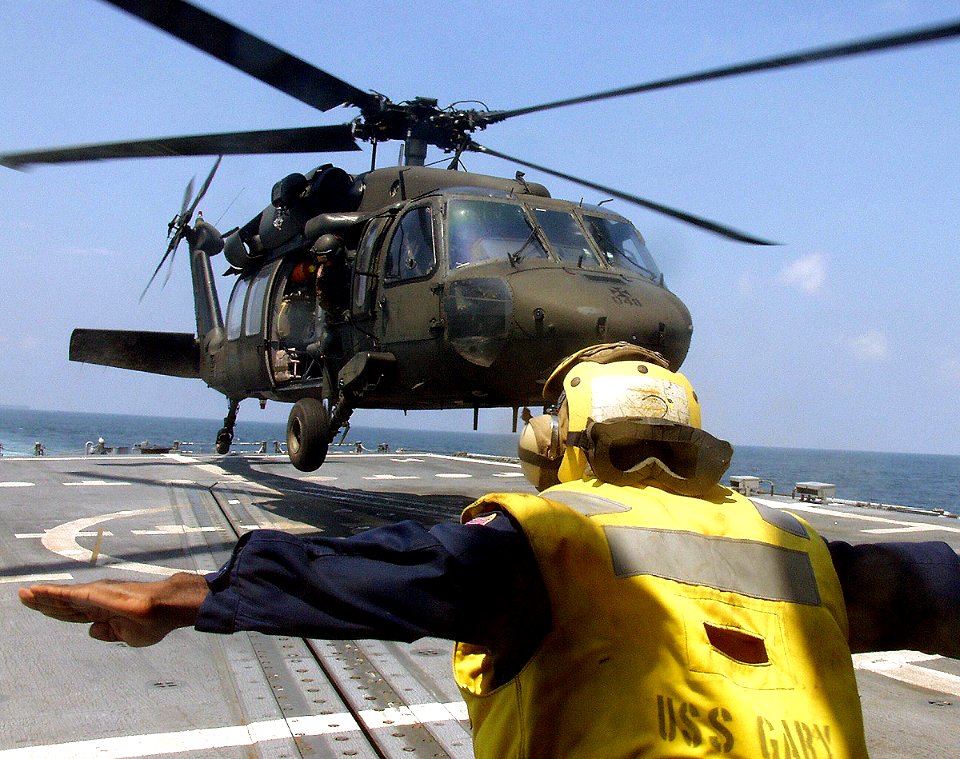 US Navy 040814-N-0000X-005 Boatswain's Mate 1st Class Tony Cloud assigned to the guided missile frigate USS Gary (FFG 51) signals a U.S. Army UH-60A Blackhawk to hover