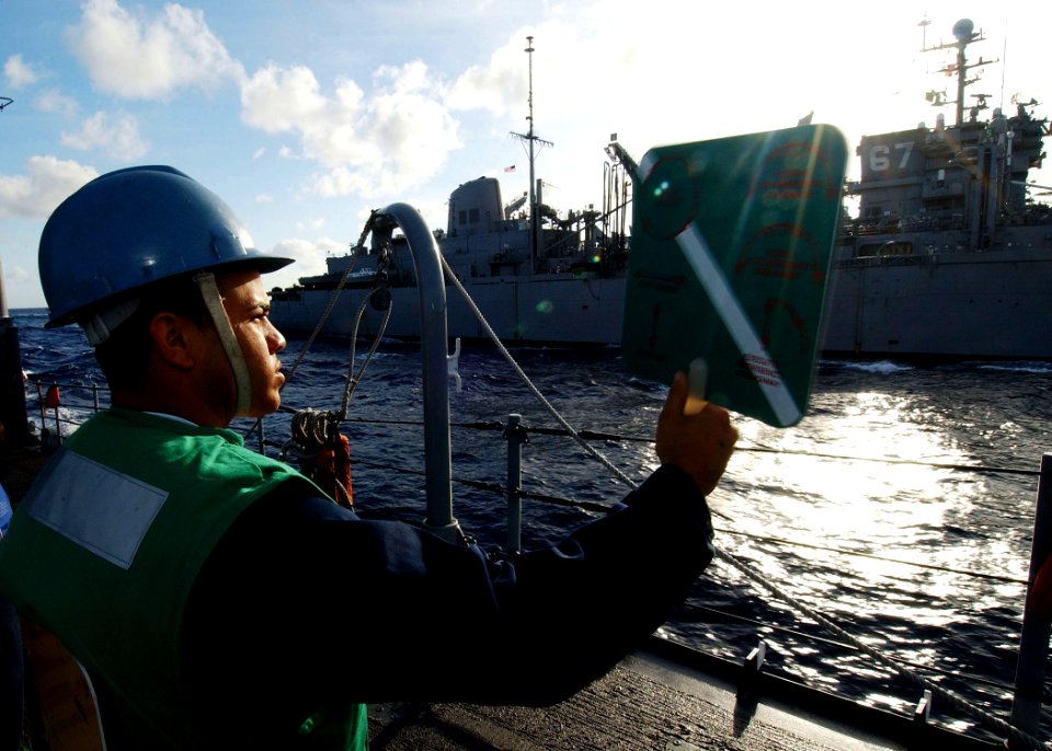 US Navy 040616-N-4374S-008 Fireman Carlos Pizarro, assigned to the guided missile cruiser USS Vicksburg (CG 69), communicates with the fast combat support ship USS Seattle (AOE 3) by signal paddles during an underway replenishm