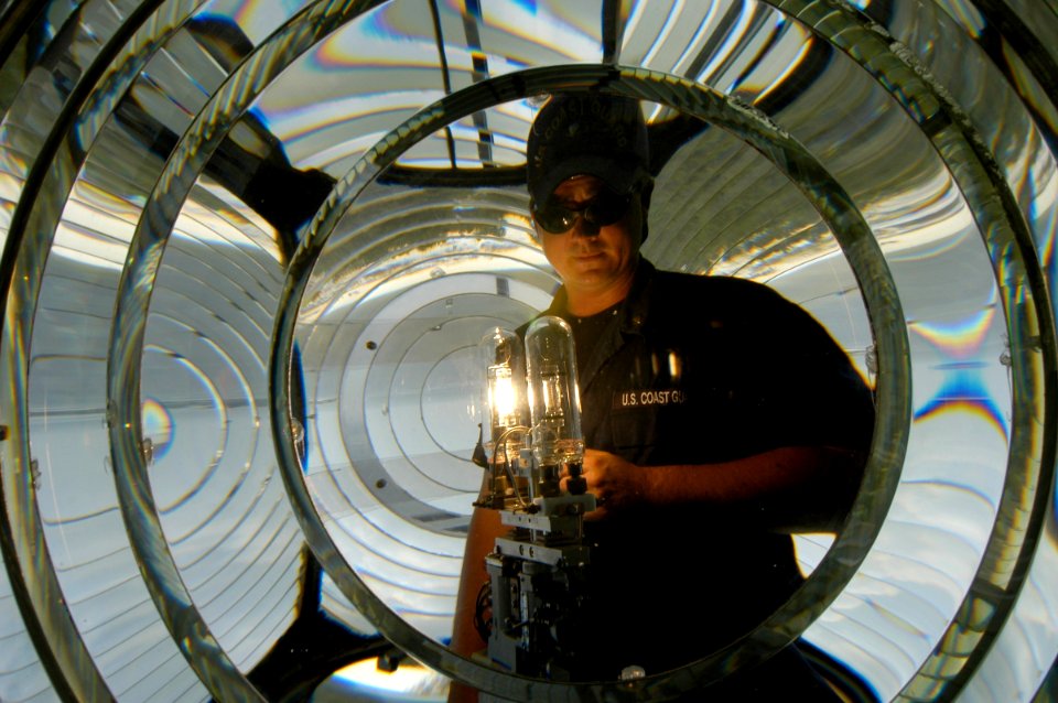 US Navy 040813-N-5328N-004 Electrician's Mate 3rd Class Ryan Pritchard looks through the center of a fresnel lens while testing a new lamp to ensure it is working properly, at the lighthouse on board Naval Air Station (NA