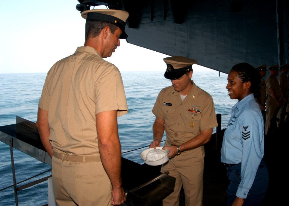 US Navy 040914-N-8704K-003 Information Systems Technician 1st Class Ebony Nichols, right, looks on as Command Master Chief Kevin Davis, center, places her white hat on the ceremonial slide