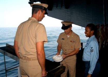 US Navy 040914-N-8704K-003 Information Systems Technician 1st Class Ebony Nichols, right, looks on as Command Master Chief Kevin Davis, center, places her white hat on the ceremonial slide