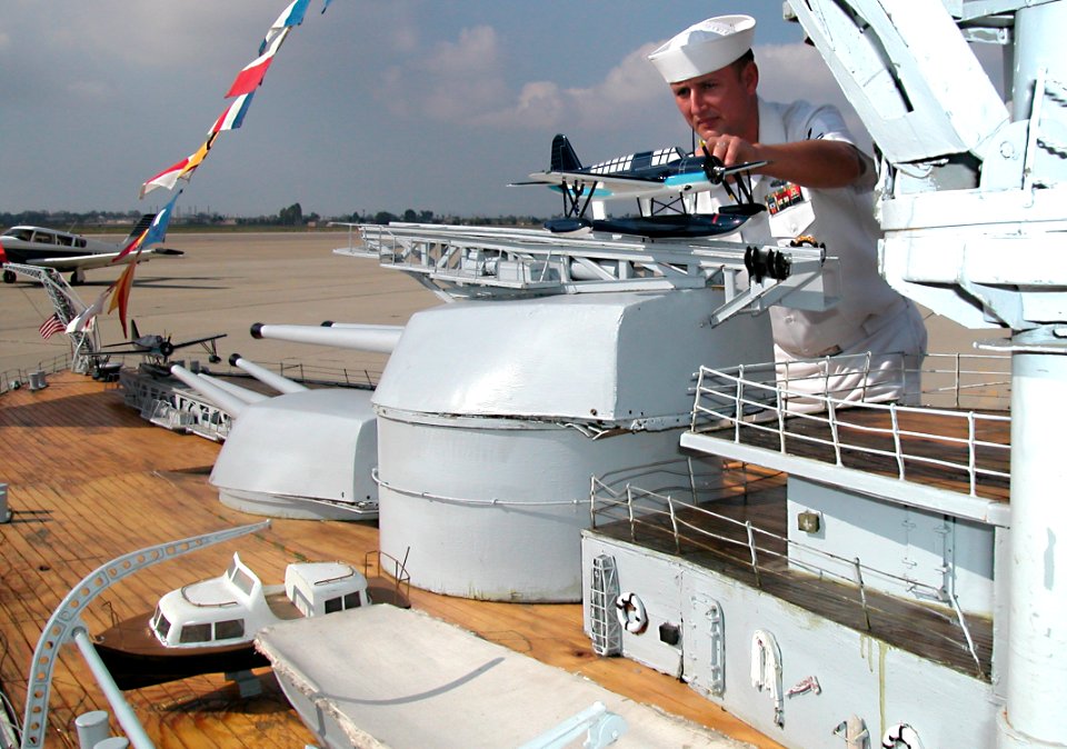 US Navy 041024-N-1159B-007 Engineman 1st Class Ronnie Choate adjusts a model of OS2U Kingfisher seaplane aboard a large-scale model of the battleship Nevada (BB 36)