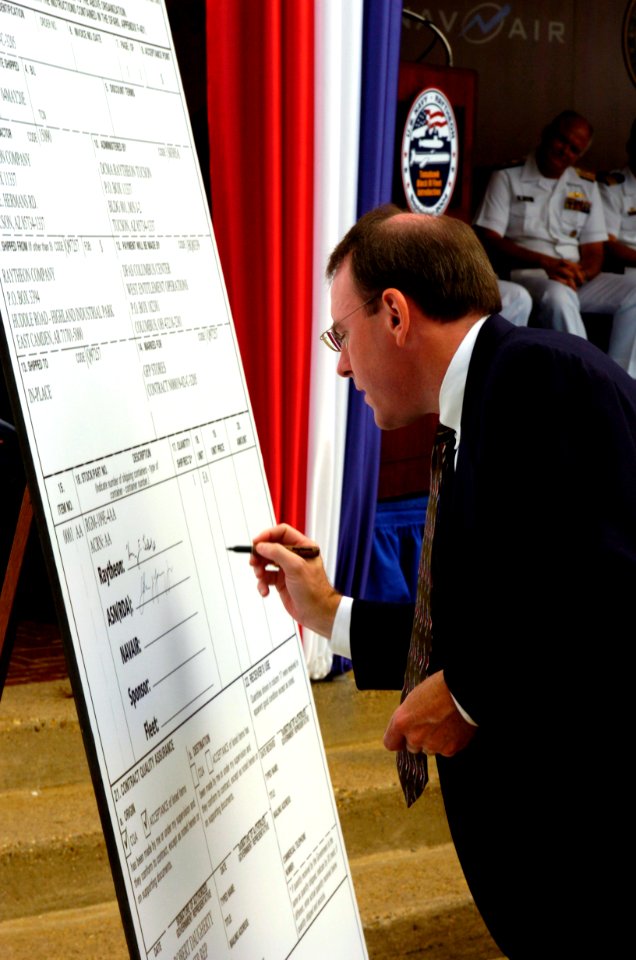 US Navy 040929-N-0295M-005 Assistant Secretary of the Navy of Research, Development and Acquisition, Mr. John J. Young Jr., formally signs a large DD250 form as the U.S. Navy formally welcomes Raytheon Company's Tomahawk