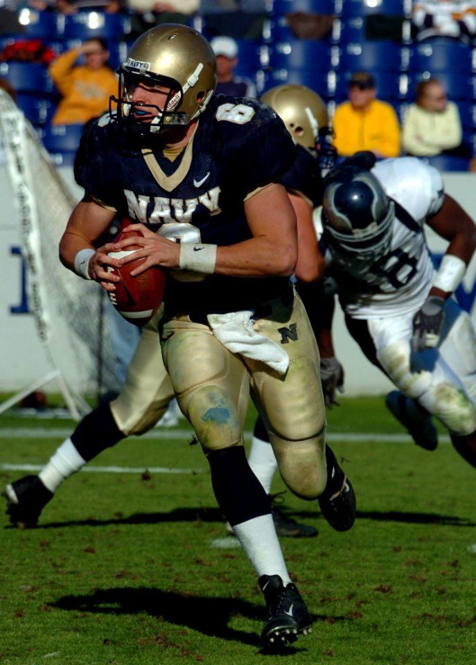 US Navy 041023-N-9693M-012 U.S. Naval Academy Midshipman Quarterback Aaron Polanco looks for a receiver downfield as a lineman blocks a Rice University defender in the background