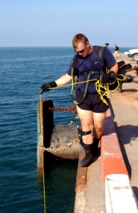 US Navy 041103-F-2760K-001 Interior Communications Electrician 3rd Class James Lester, assigned to Explosive Ordnance Disposal Mobile Unit Eight (EODMU-8), Detachment Eighteen, holds a line attached to submerged divers