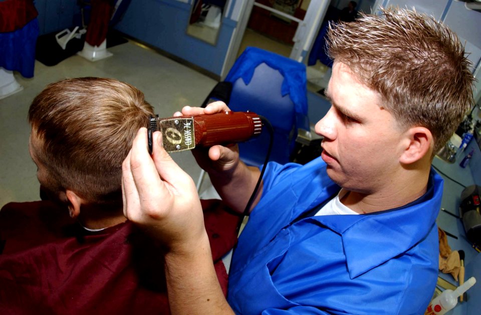US Navy 041031-N-8158F-113 Ship's Serviceman 3rd Class Ben Quail, of Phoenix, Ariz., gives Storekeeper 3rd Class Jonathan Towsley, of South Hills, Mich., a haircut in the barbershop aboard the aircraft carrier USS Nimitz