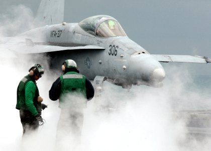 US Navy 041201-N-5345W-014 Flight deck personnel are surrounded by steam escaping from the steam-powered catapult while an approaching F-A-18C Hornet assigned to the Bulls of Strike Fighter Squadron Three Seven (VFA-37) prepare