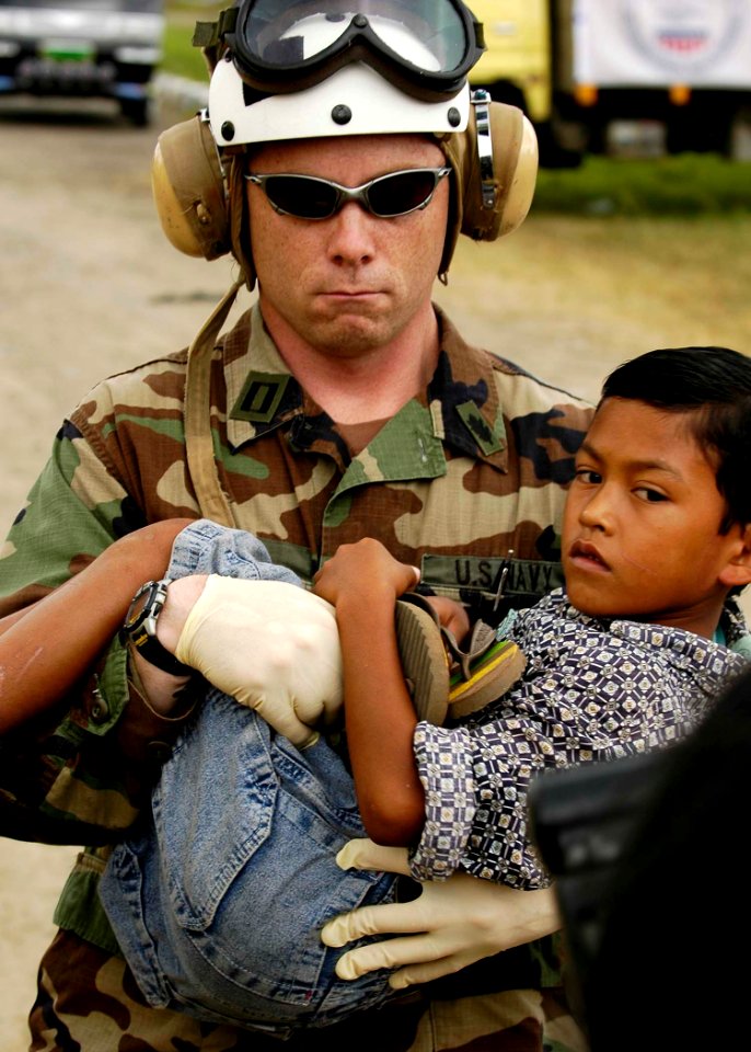 US Navy 050106-N-4166B-287 Lt. Shawn Harris, assigned to the guided missile destroyer USS Shoup (DDG 86), carries an injured boy from an MH-60S Knighthawk helicopter to a triage site