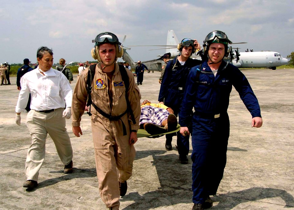 US Navy 050103-N-0057P-462 Sailors assigned to USS Abraham Lincoln (CVN 72) and embarked Carrier Air Wing Two (CVW-2), carry a refugee off an SH-60B Seahawk en route to the U.S. Medical tent for treatment in Aceh, Sumatra, Indo