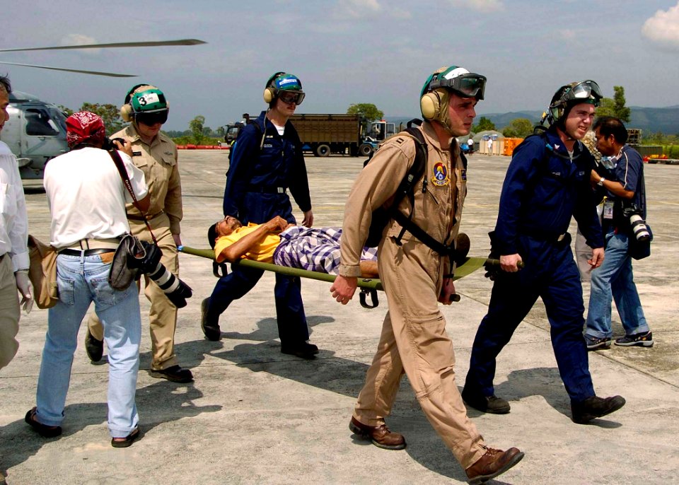 US Navy 050103-N-0057P-460 Sailors assigned to USS Abraham Lincoln (CVN 72) and embarked Carrier Air Wing Two (CVW-2), carry a refugee off an SH-60B Seahawk en route to the U.S. Medical tent for treatment in Aceh, Sumatra, Indo