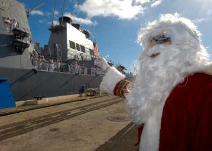 US Navy 041209-N-3019M-005 A family member dressed in a Santa Claus costume waves an American flag as the Arleigh Burke-class guided missile destroyer USS Hopper (DDG 70) returns to Pearl Harbor, Hawaii