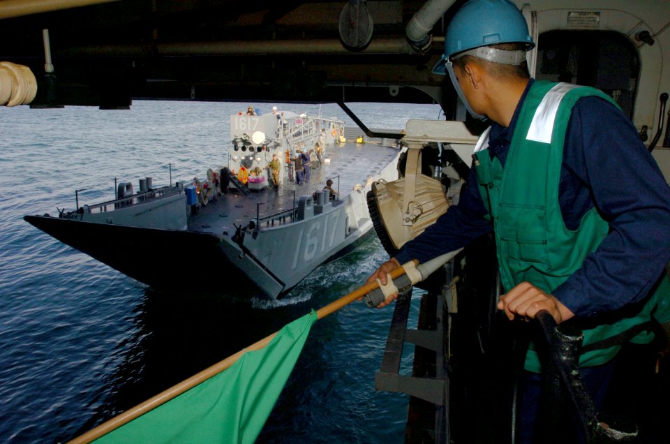 US Navy 050126-N-9866B-014 Seaman Alexis Lerma gives a signal to a landing craft utility (LCU) to pull inside the amphibious assault ship USS Peleliu (LHA 5) during amphibious assault training