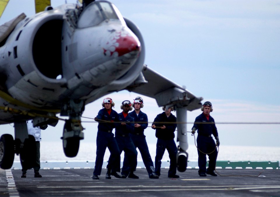 US Navy 050217-N-9866B-001 Aviation Boatswain's Mates work together to provide guidance to a AV-8A Harrier training aircraft as the aircraft is hoisted in the air during a flight deck training drill aboard the amphibious assaul
