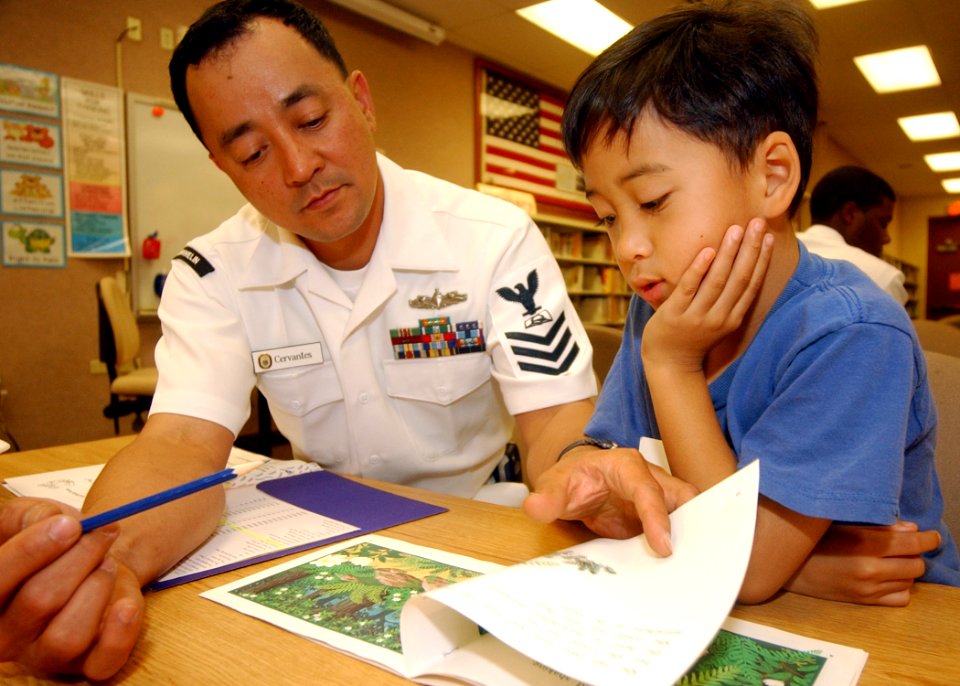 US Navy 050222-N-3019M-001 Culinary Specialist 1st Class Davidson Cervantes, assigned to the guided missile frigate USS Crommelin (FFG 37), helps a child read a book at Holomua Elementary School in Ewa Beach, Hawaii
