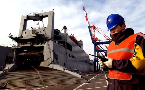 US Navy 050312-F-2902B-025 A Korean contractor uses a radio to contact his co-workers while loading a U.S. Army tracked vehicles aboard the Military Sealift Command (MSC) roll-on-roll-off shop USNS Watson (T-AKR 310)