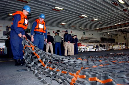 US Navy 050302-N-9866B-004 Two Sailors assigned to the Deck Department layout a cargo net in the hanger bay aboard the amphibious assault ship USS Peleliu (LHA 5) in preparation for the ship pulling back into Naval Station San