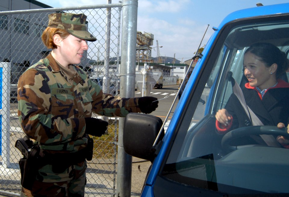US Navy 050308-N-2385R-029 Master-at-Arms Seaman Carly Farmer checks an identification card (ID) before allowing a driver to enter the gate at U.S. Fleet Activities Sasebo, Japan