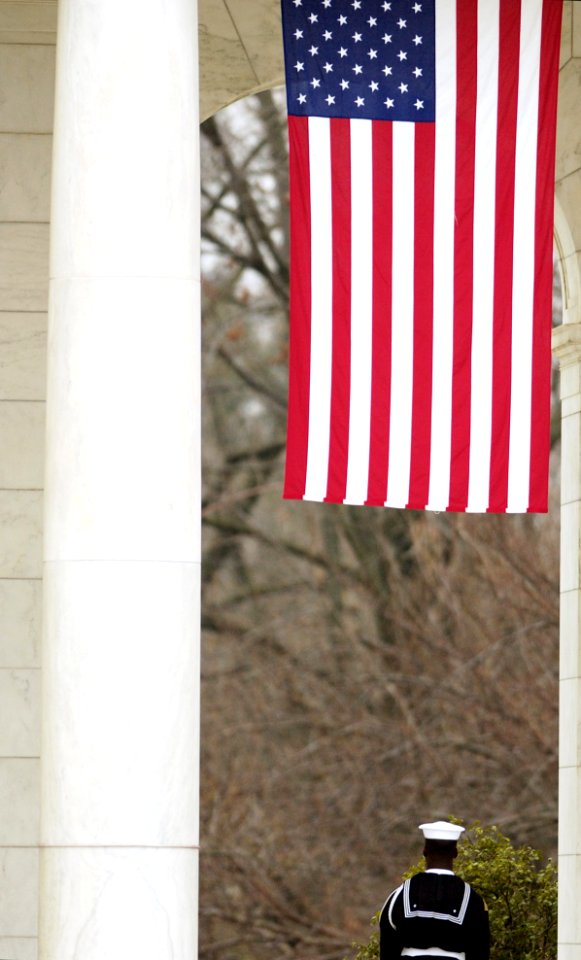 US Navy 050327-F-7466S-063 A member of the Navy Honor Guard stands under a large American Flag during the Joint Force Headquarters-National Capital Region's Easter Sunrise Service