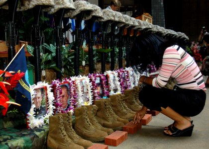 US Navy 050307-N-3019M-002 A family member kneels before a ceremonial formation of U.S. Marine Corps infantry equipment during the First Battalion, Third Marine's Memorial Service at the Hawaii State Capitol Building in P