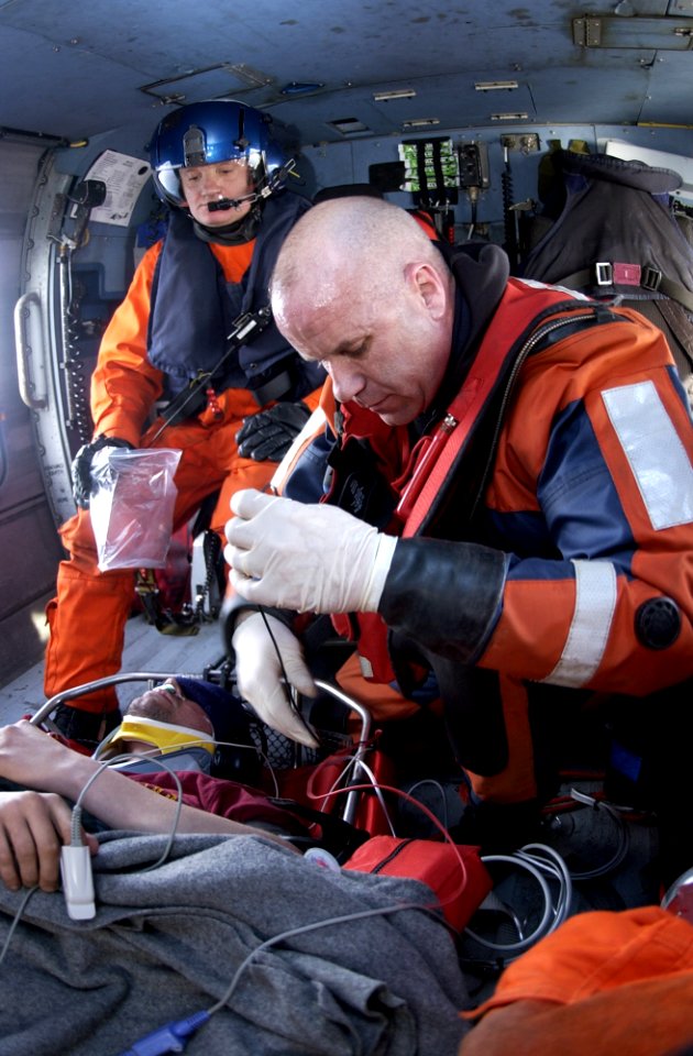 US Navy 050317-C-0000L-001 U.S. Coast Guard Petty Officer 1st Class Brian Laubenstein, a rescue swimmer assigned to Coast Guard Air Station Cape Cod, right, monitors an injured fisherman's vitals inside the cabin of an HH-60 Ja
