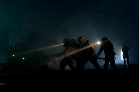 US Navy 050317-N-9866B-003 A fire fighting team works in the darkness to put out a simulated fire in the hanger bay of the amphibious assault ship USS Peleliu (LHA 5) during a mass conflagration drill
