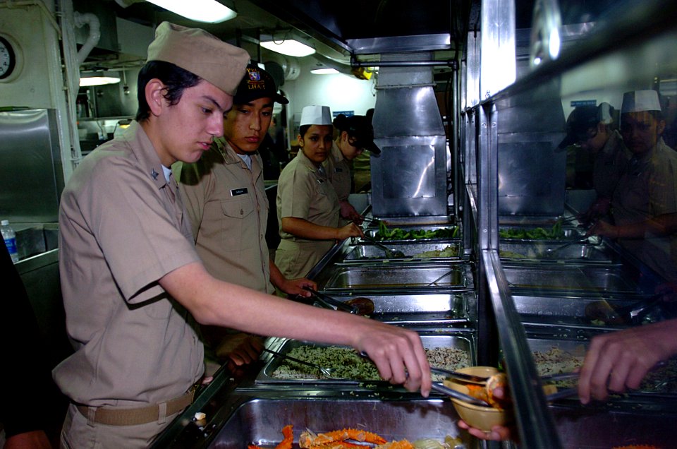 US Navy 050407-N-9866B-004 Naval Junior Reserve Officers Training Corps (NJROTC) Petty Officer 3rd Class Jose Lira serves crab legs in the mess lines to Sailors aboard the amphibious assault ship USS Peleliu (LHA 5)