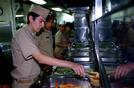 US Navy 050407-N-9866B-004 Naval Junior Reserve Officers Training Corps (NJROTC) Petty Officer 3rd Class Jose Lira serves crab legs in the mess lines to Sailors aboard the amphibious assault ship USS Peleliu (LHA 5)