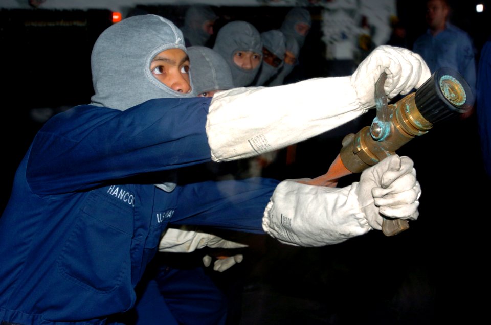 US Navy 050311-N-9866B-006 Electrician's Mate Fireman Apprentice Hermes Hancock sways the nozzle of a fire fighting hose back and forth to put out a simulated fire in the ship's hangar bay aboard