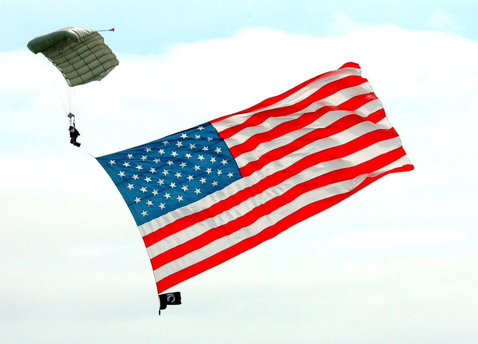 US Navy 050416-N-0295M-104 A member of the Red Baron Pizza Squadron parachutes down to show center carrying a huge American Flag at the start of the 2005 Coastal Carolina Air Show in Wilmington, N.C