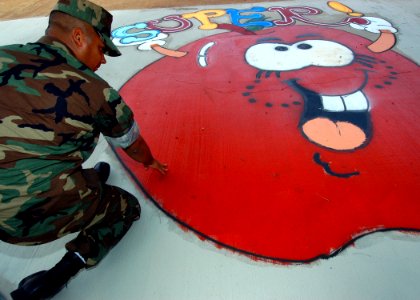US Navy 050401-N-3019M-001 Boatswain's Mate 2nd Class Ricardo Valverde, assigned to Mobile Diving Salvage Unit One (MDSU-1), inspects a sidewalk graphic design he painted for children at Waipahu Elementary School