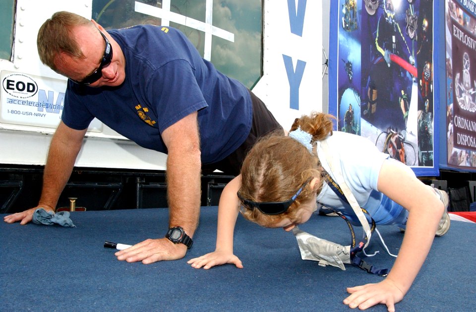 US Navy 050529-N-4729H-109 Senior Chief Aviation Ordnanceman Ron Mitchell, a recruiter for the Navy Explosive Ordnance Disposal (EOD) community, shows a young fan how to do a Navy push-up
