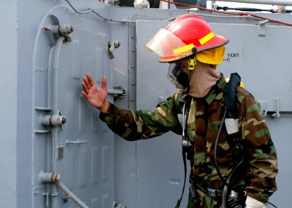 US Navy 050603-N-2385R-103 Seaman Jose Cadiz assigned to Assault Craft Unit One (ACU-1), simulates checking for heat on a hatch during his role as investigator for a General Quarters (GQ) drill