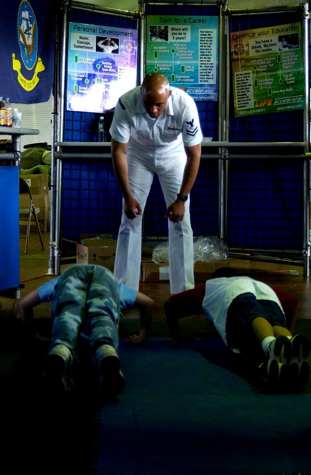 US Navy 050530-N-5637H-003 Naval Reservist, Master-at-Arms 2nd Class David Coleman, instructs two young kids as they perform push-ups for posters at the Navy Recruiting District New York display