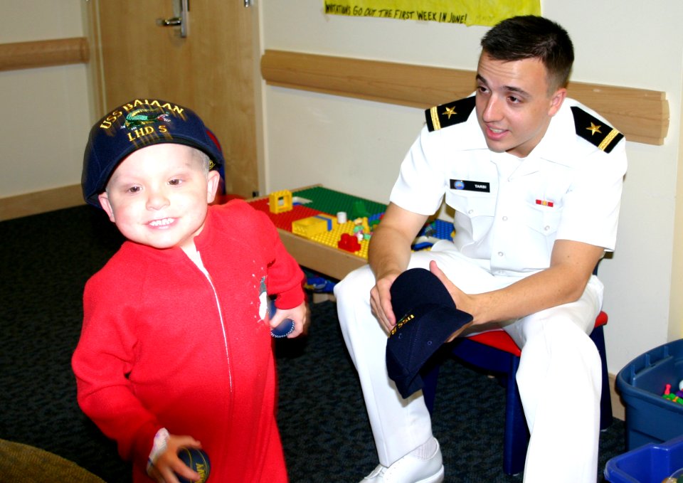 US Navy 050616-N-8110K-048 Boston College graduate, Ens. Luke Tarby presents a ball cap to a young child during Caps for Kids visit