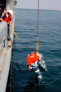 US Navy 050618-N-1464F-005 U.S. Navy civilian contractor Nate Kibbler, top left, lowers Dave Diepenhorst into the water in an Atmospheric Diving System (ADS 2000) from the salvage ship USS Grasp (ARS 51)