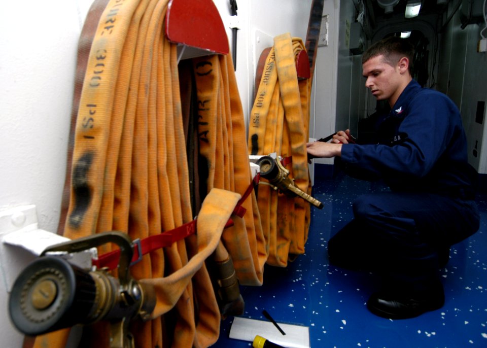 US Navy 050708-N-1397H-002 Aviation Electronics Technician 3rd Class Brad Delabruere assigned to the amphibious assault ship USS Peleliu (LHA 5) restores a fire hose after completing periodic maintenance on a fire station