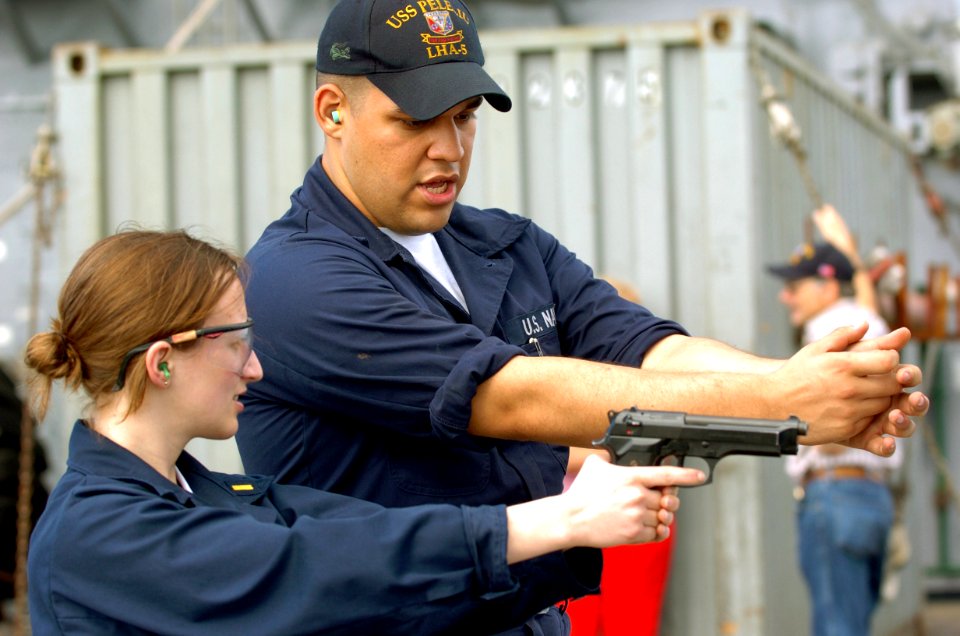 US Navy 050625-N-9866B-021 Gunner's Mate Seaman Roberto Echevarria instructs Ens. Sarah Kolb on how to fire a 9mm handgun
