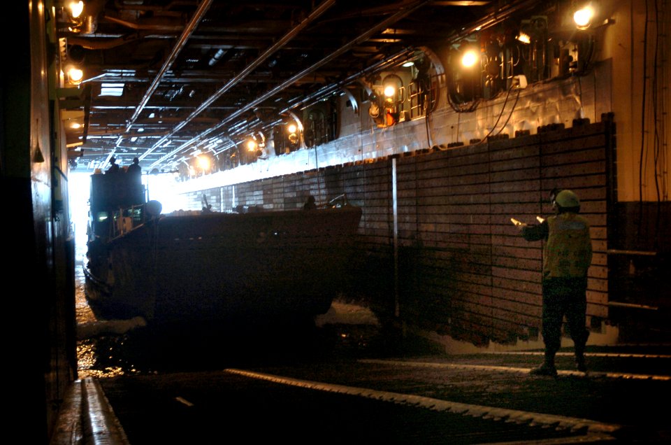 US Navy 050719-N-9866B-055 Seaman Kevin Bull directs a landing craft, utility (LCU) out of the well deck of the amphibious assault ship USS Peleliu (LHA 5) during an ammunition on load