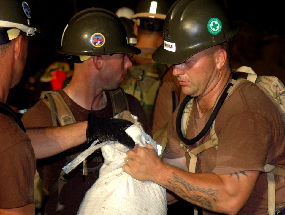 US Navy 050924-N-0000X-001 U.S. Navy Builder 1st Class Daniel McKee, right, assigned to Naval Mobile Construction Unit Four Zero (NMCB-40), hands-off a sandbag to another Seabee while repairing a levee