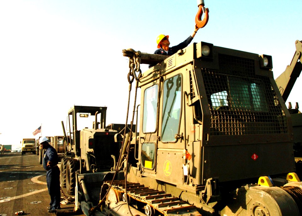 US Navy 051018-N-0716S-002 A Sailor assigned to the dock landing ship USS Pearl Harbor (LSD 52), attaches a crane hook to a heavy bulldozer in order to unload it from the flight deck of the ship in Karachi, Pakistan