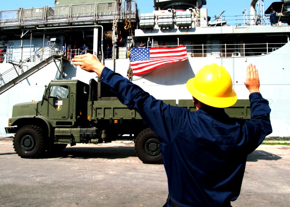 US Navy 051018-N-0716S-008 U.S. Navy Boatswain's Mate 2nd Class Galen Roberts directs a crane carrying a 7-ton dump truck while unloading supplies from the flight deck of the dock landing ship USS Pearl Harbor (LSD 52)