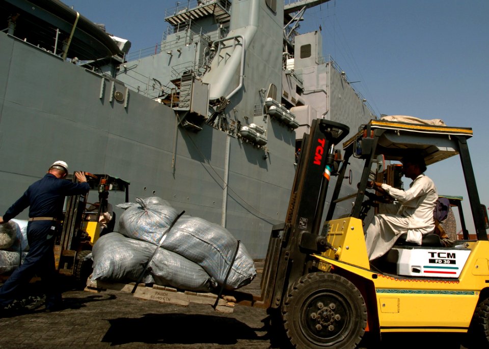 US Navy 051024-N-0716S-007 A U.S. Navy chief petty officer, left, assigned to the dock landing ship USS Pearl Harbor (LSD 52), guides a Pakistani forklift operator as he transports a load of relief supplies on the pier in Kara